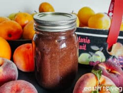 A mason jar full of rhubarb butter surrounded by fresh summer fruit.