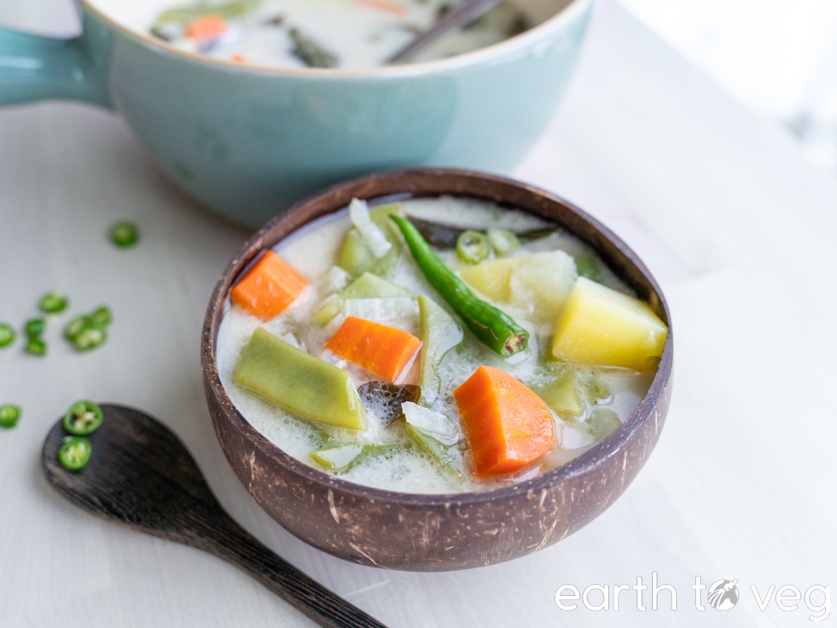 a bowl full of kerala ishtew coconut stew sitting on a wooden table beside a green dutch oven