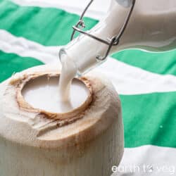 Coconut milk is poured from a glass bottle into a hollowed-out coconut shell.